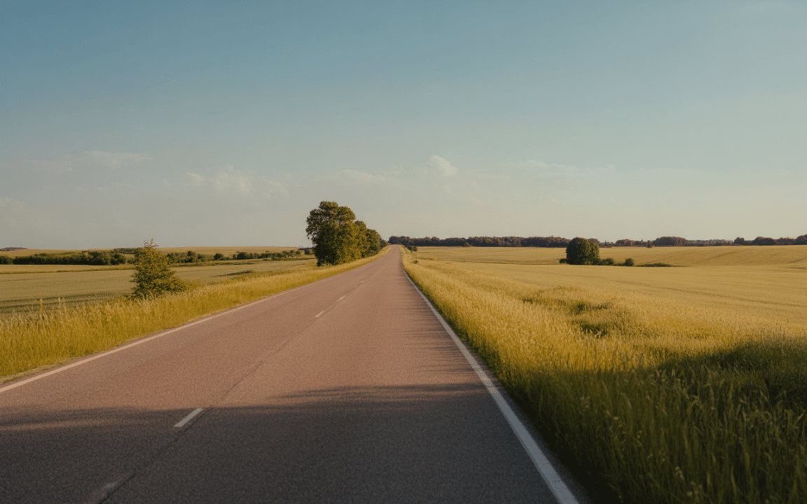 Une route asphaltée s'étend droit devant, flanquée de champs verdoyants sous un ciel bleu ensoleillé.