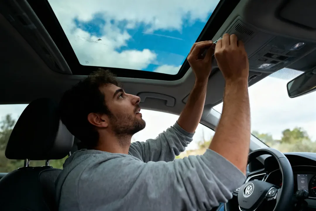 Homme installant équipement dans une voiture Volkswagen, regardant à travers le toit panoramique ouvert.