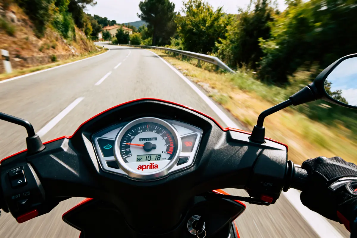 Motard conduisant une moto Aprilia sur une route sinueuse entourée de végétation, vue depuis le guidon.