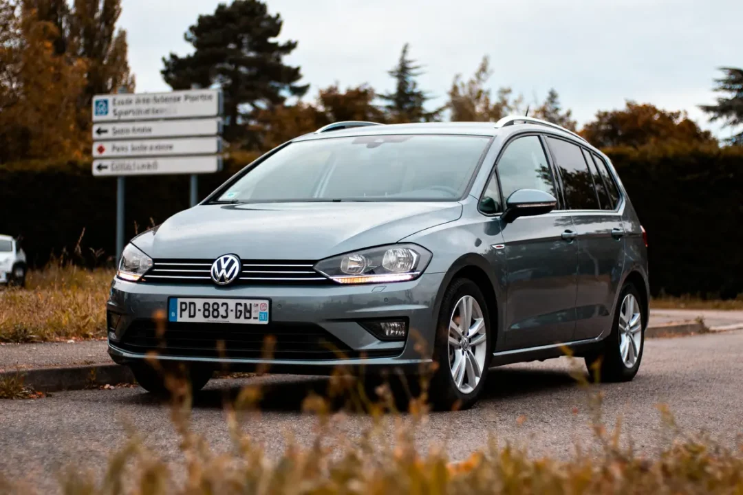 Voiture Volkswagen grise stationnée sur une route avec panneau directionnel à l'arrière-plan. Environnement naturel.