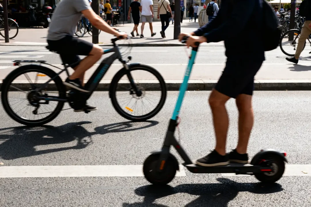 Un cycliste et un utilisateur de trottinette roulent sur une rue animée en ville.