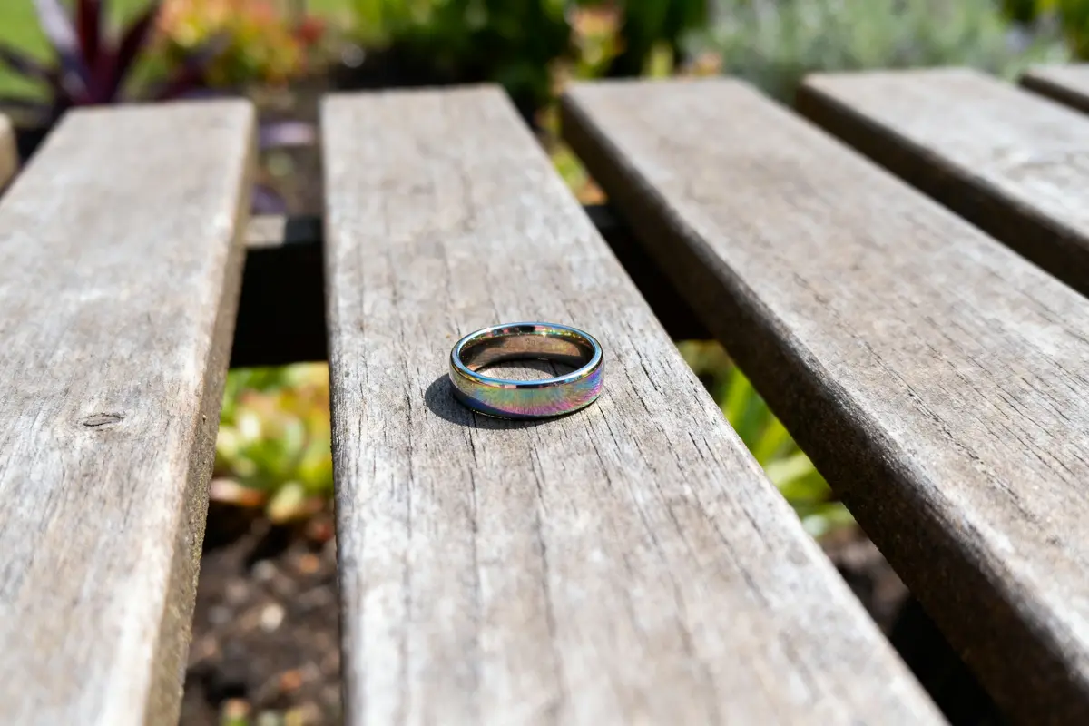 Anneau irisé posé sur une table en bois, avec fond flou de plantes.