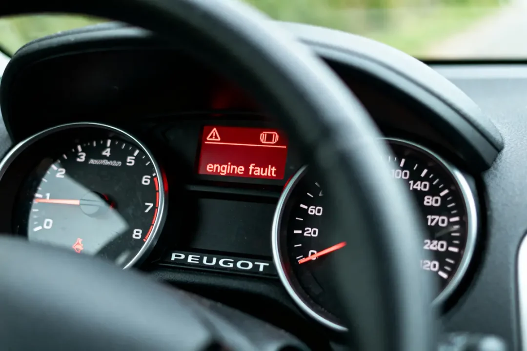 Tableau de bord Peugeot avec avertissement "engine fault", entouré des jauges de vitesse et de régime moteur.