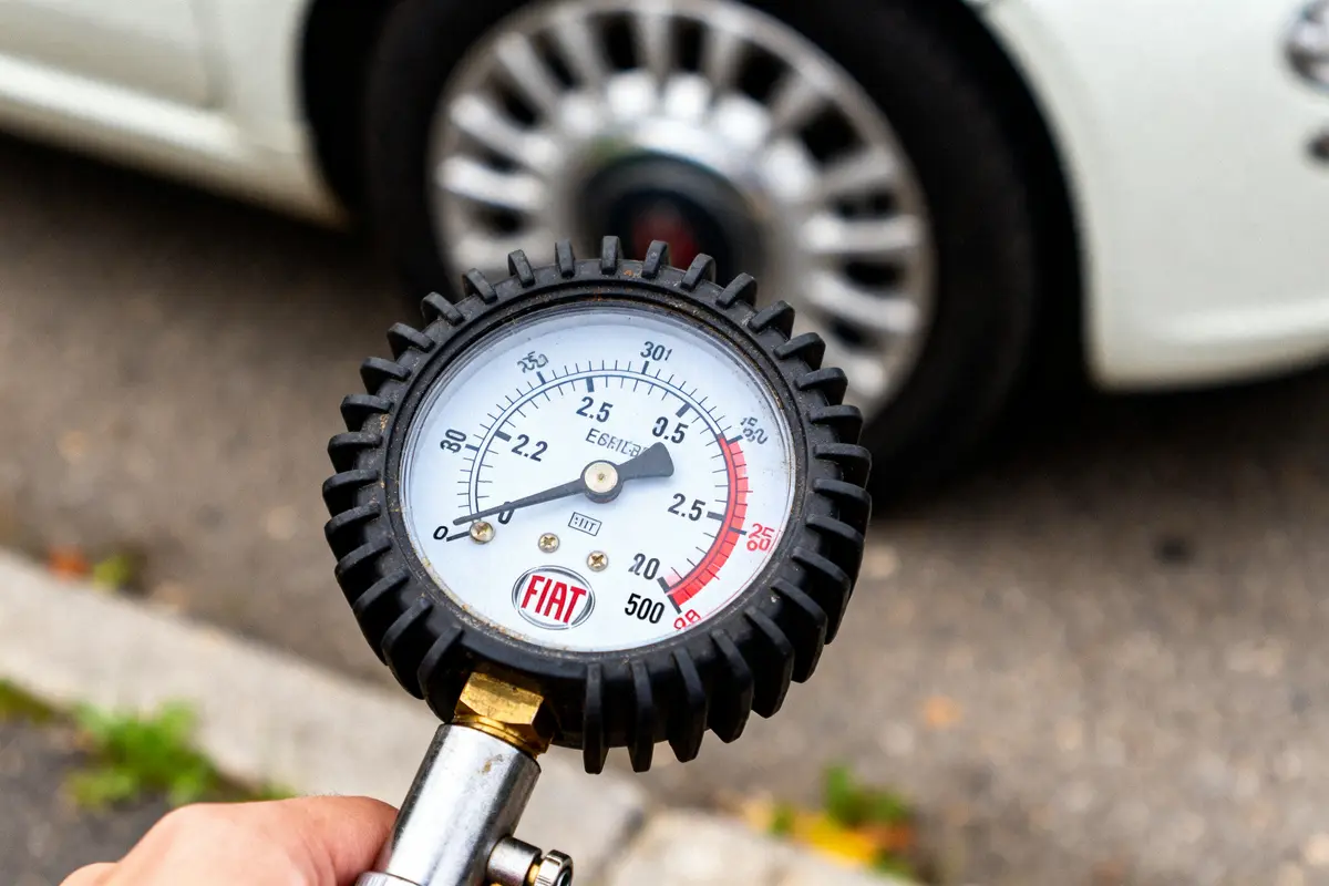 Manomètre Fiat mesurant la pression d'un pneu devant une voiture blanche sur la route.