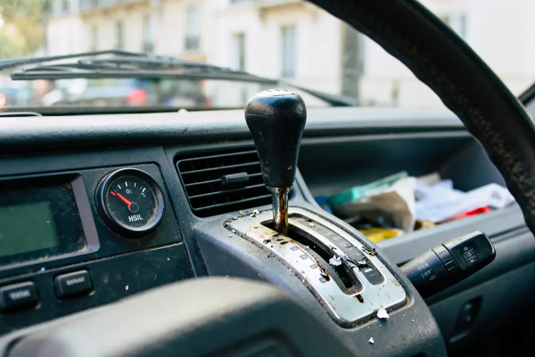 Levier de vitesse automatique usé dans l’habitacle d'une voiture avec désordre à l'arrière.