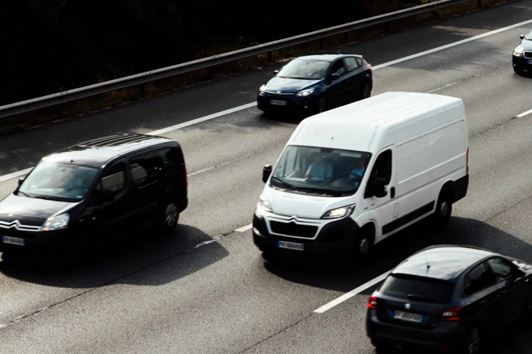 Voitures et camionnette circulant sur autoroute à trois voies avec glissière de sécurité.