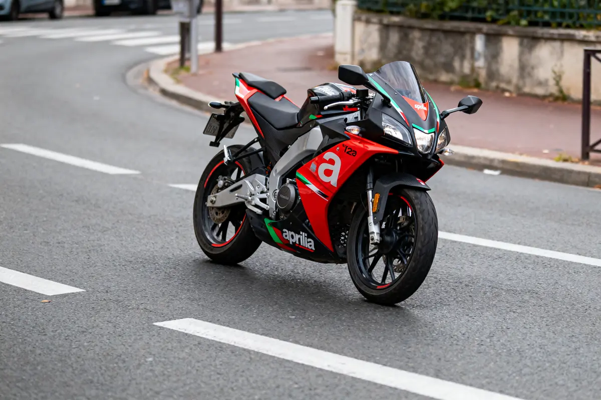 Moto sportive Aprilia rouge et noire stationnée sur une route urbaine.