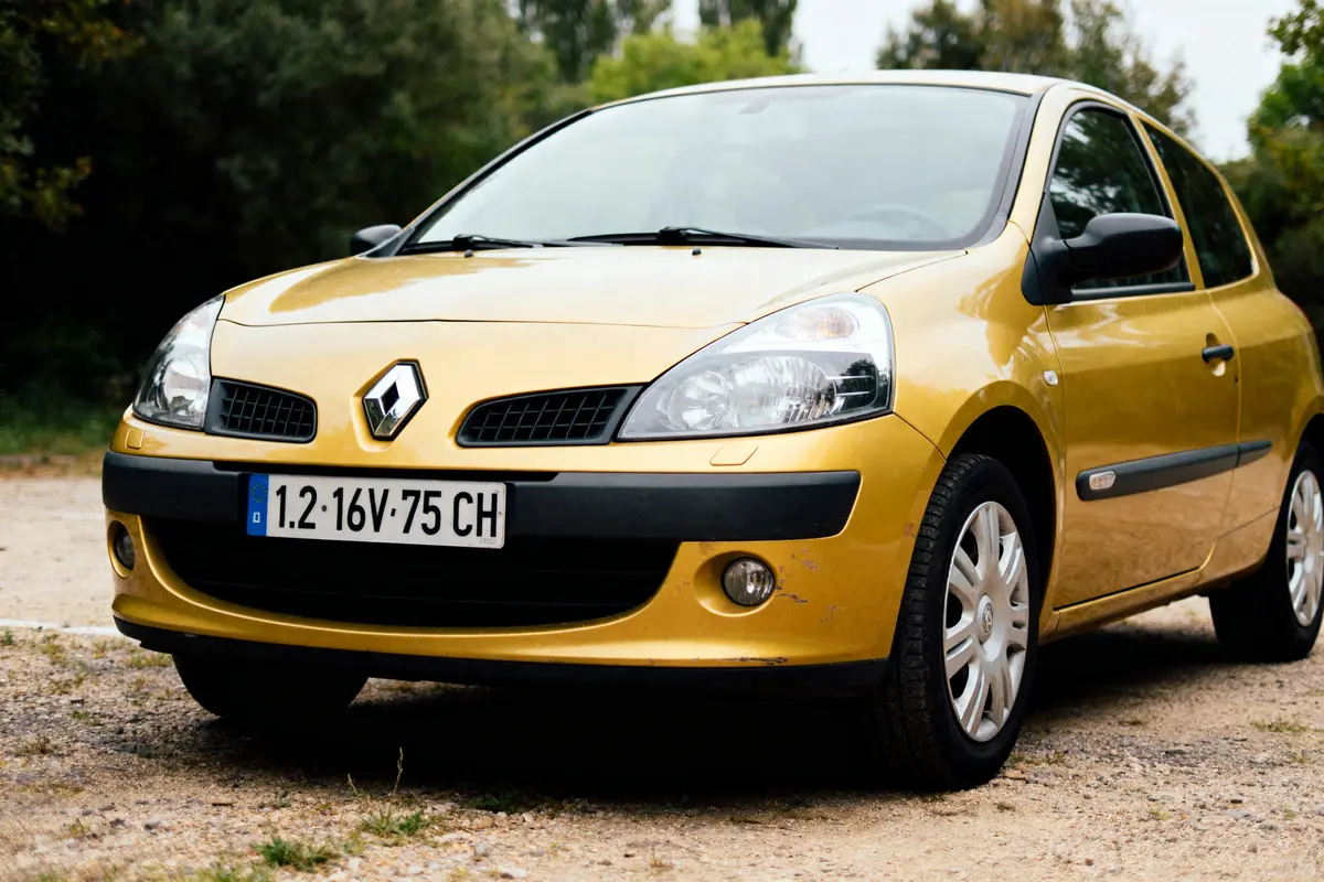 Voiture Renault Clio jaune garée à l'extérieur, immatriculation visible, arbres en arrière-plan.