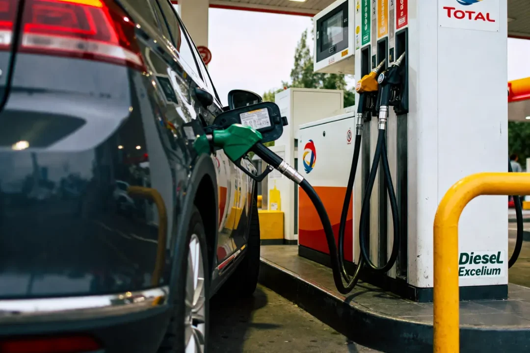 Voiture noire se fait ravitailler en carburant dans une station-service Total. Pompe et pistolet verts.
