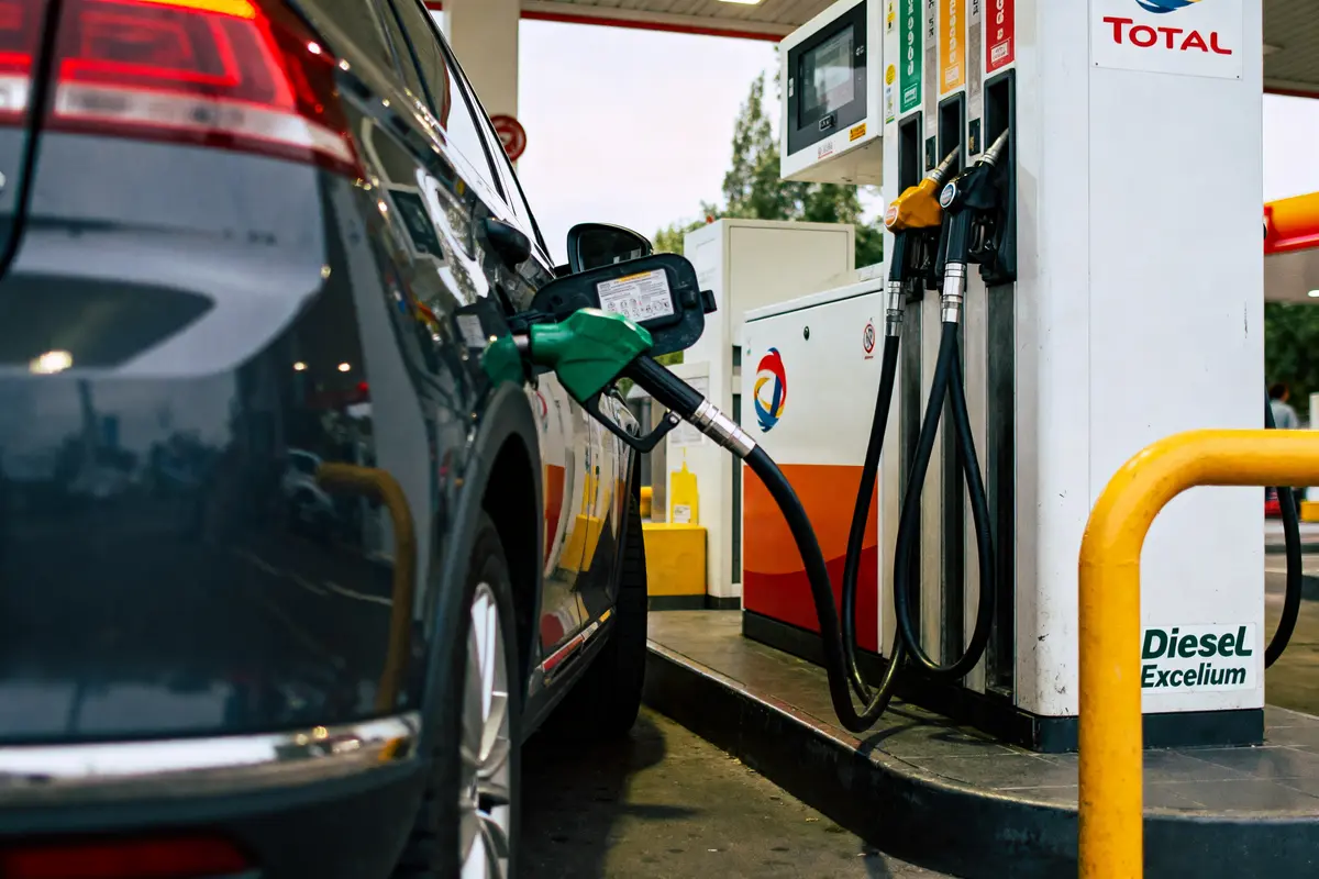 Voiture noire se fait ravitailler en carburant dans une station-service Total. Pompe et pistolet verts.