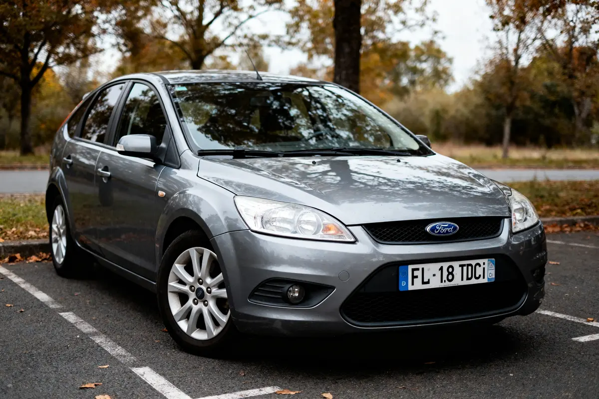 Voiture grise Ford Focus garée, arbres et feuilles d'automne visibles en arrière-plan. Plaque: FL-18 TDCi.