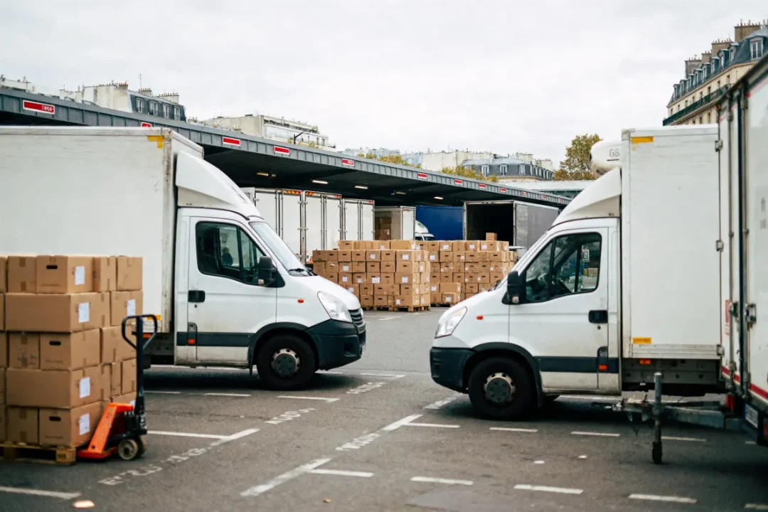 Des camionnettes blanches stationnées près de cartons empilés dans un entrepôt urbain.