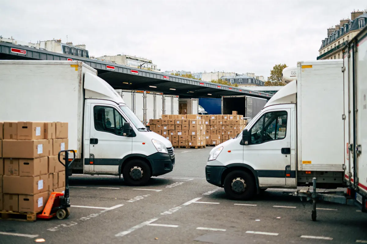 Des camionnettes blanches stationnées près de cartons empilés dans un entrepôt urbain.