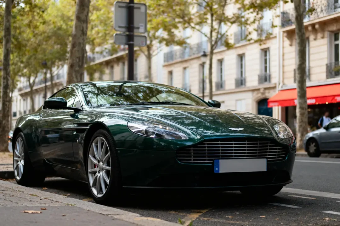 Voiture de luxe verte garée dans une rue bordée d'arbres et de bâtiments parisiens.
