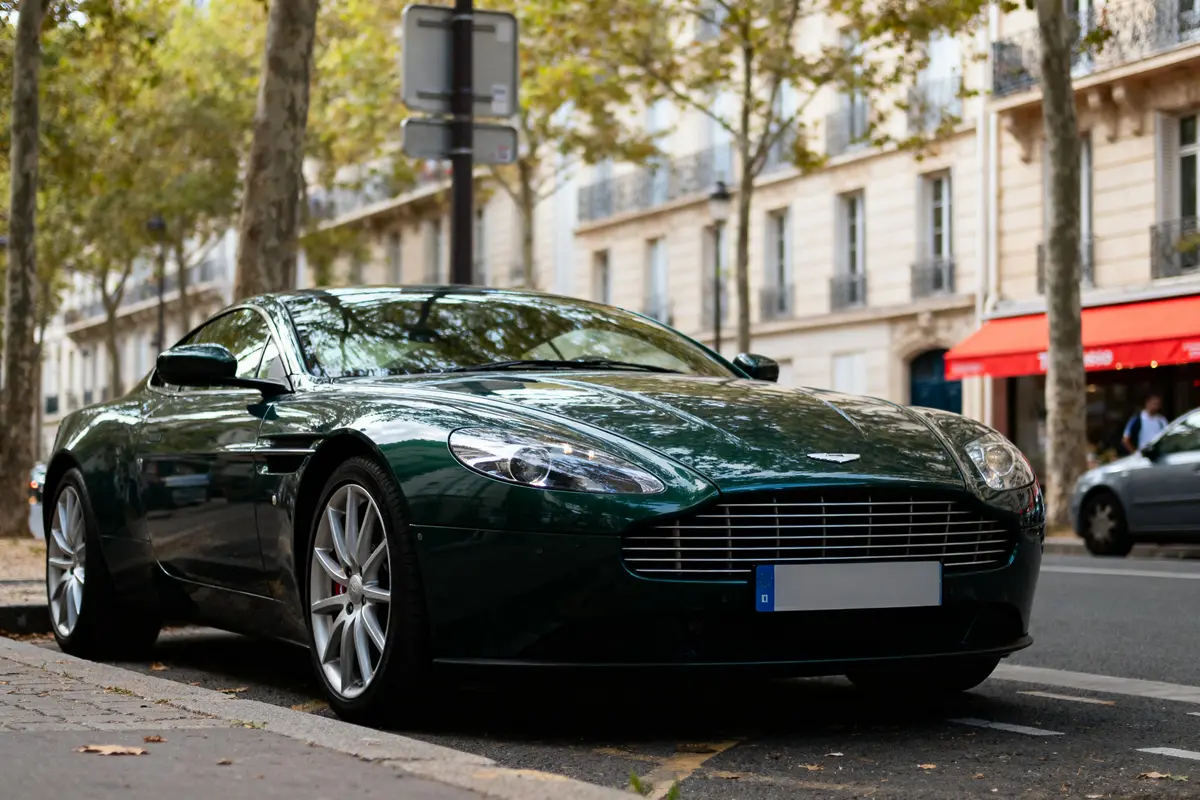Voiture de luxe verte garée dans une rue bordée d'arbres et de bâtiments parisiens.