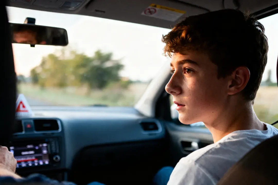 Jeune passager à l'arrière d'une voiture regardant vers l'avant, éclairé par la lumière du jour.