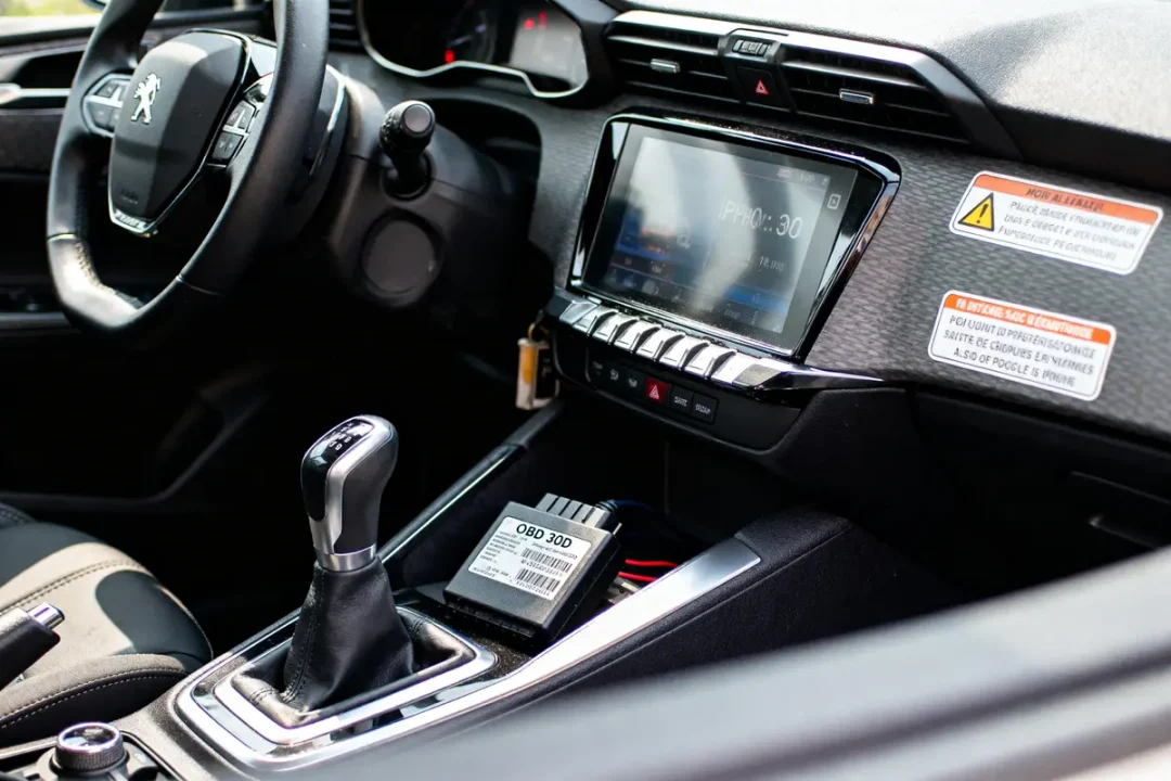 Intérieur de voiture Peugeot avec écran tactile, levier de vitesse, volant et un dispositif OBD sur la console.