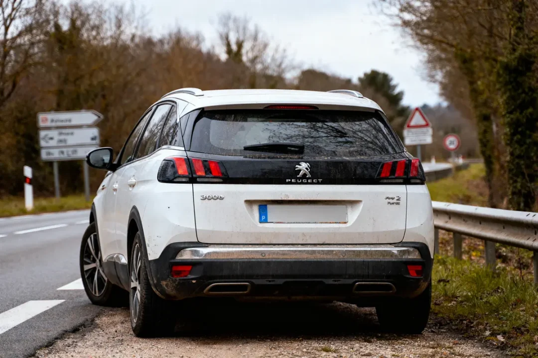 SUV blanc Peugeot garé en bordure de route, panneau de signalisation visible derrière.