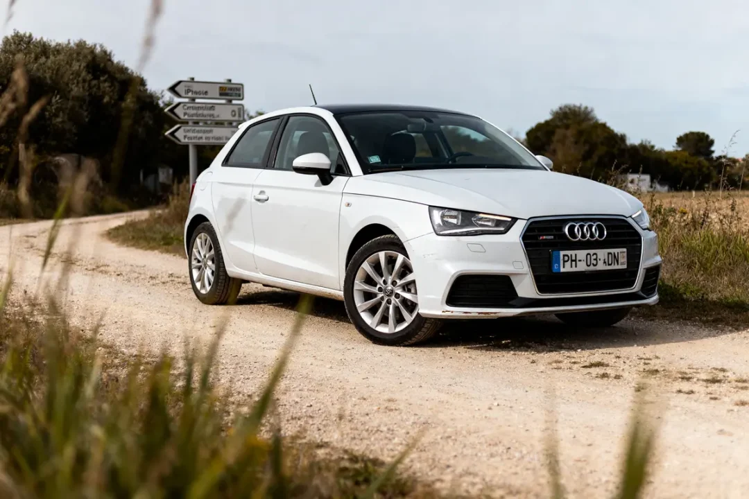 Audi A1 d'occasion blanche sur chemin de terre devant panneau directionnel en campagne