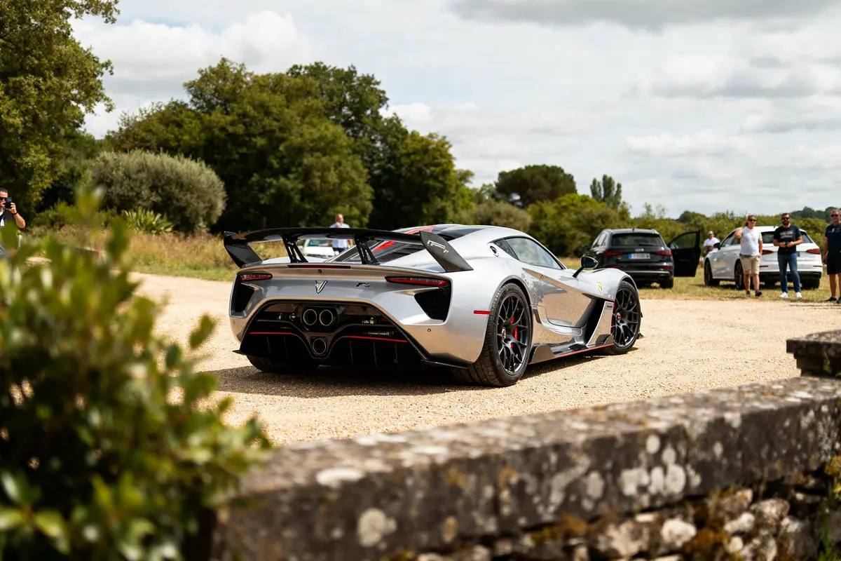 Voiture sportive Hennessey Venom F5 grise sur un chemin de campagne avec spectateurs.