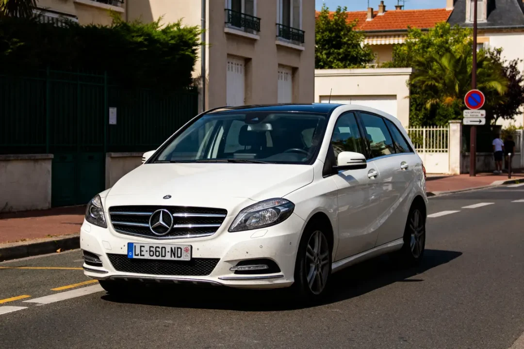 Voiture blanche Mercedes Classe B stationnée dans une rue résidentielle ensoleillée