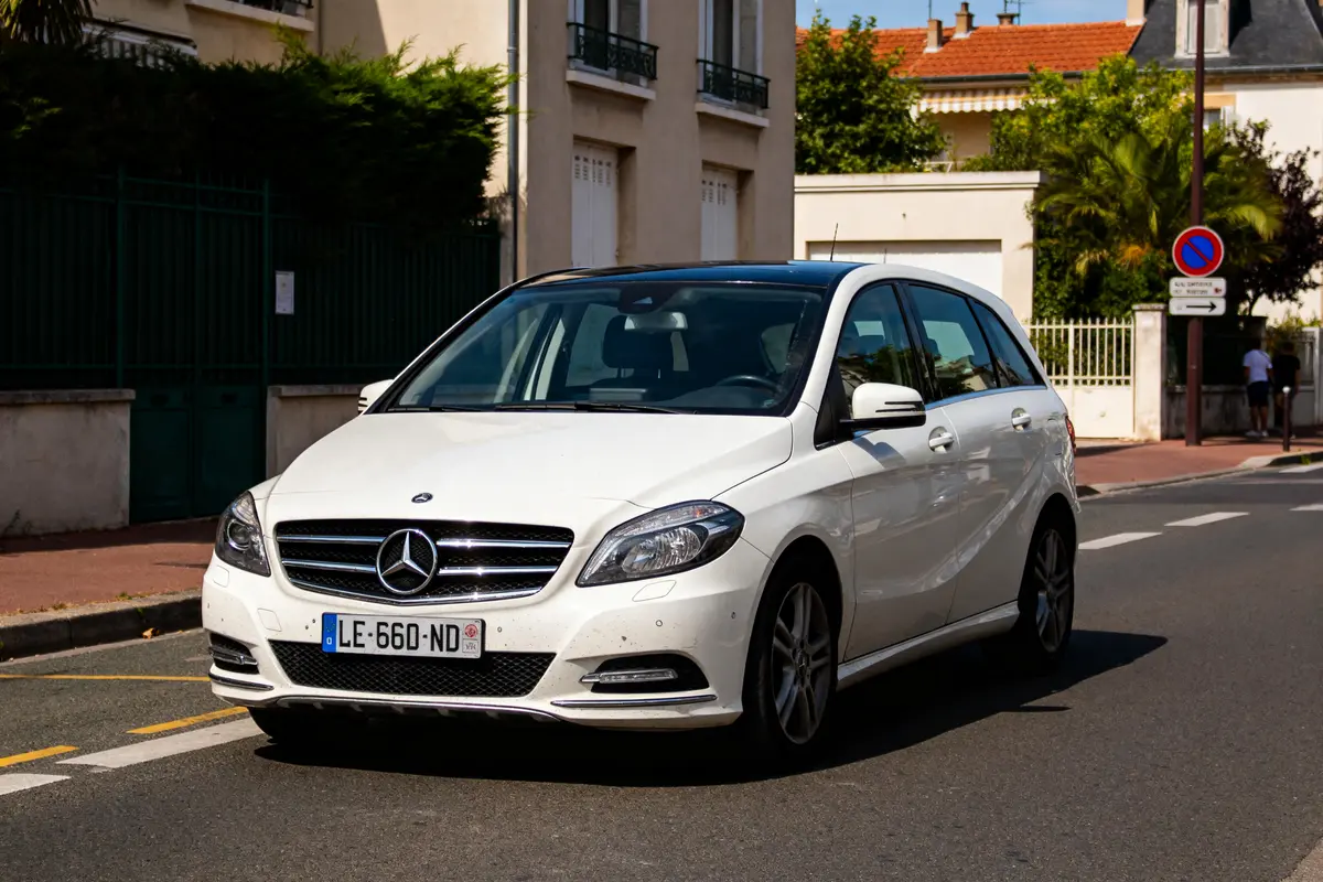 Voiture blanche Mercedes Classe B stationnée dans une rue résidentielle ensoleillée