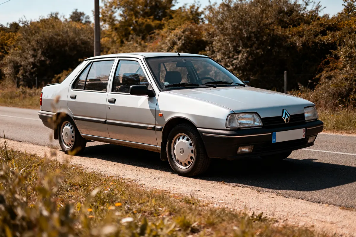 Renault 21 Sedan argentée garée sur une route de campagne en été