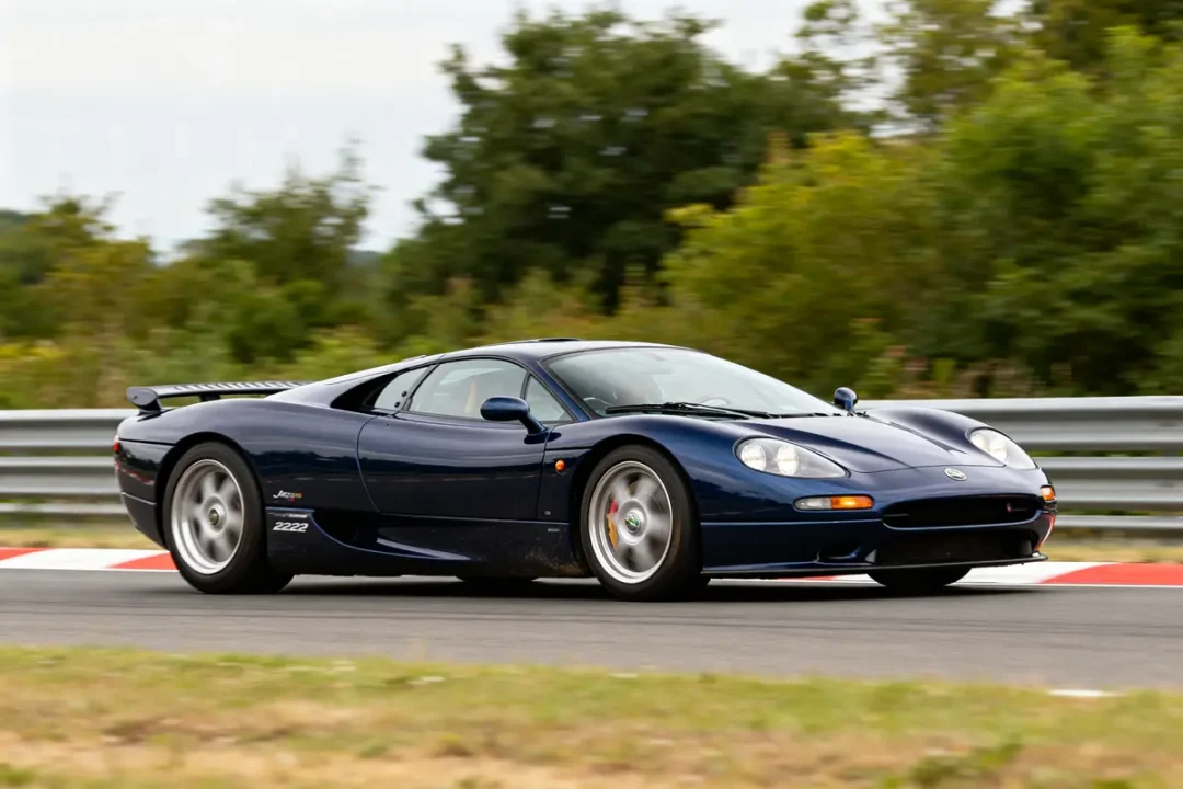 Supercar Jaguar XJ220 bleue sur circuit avec arbres en arrière-plan et garde-corps métallique