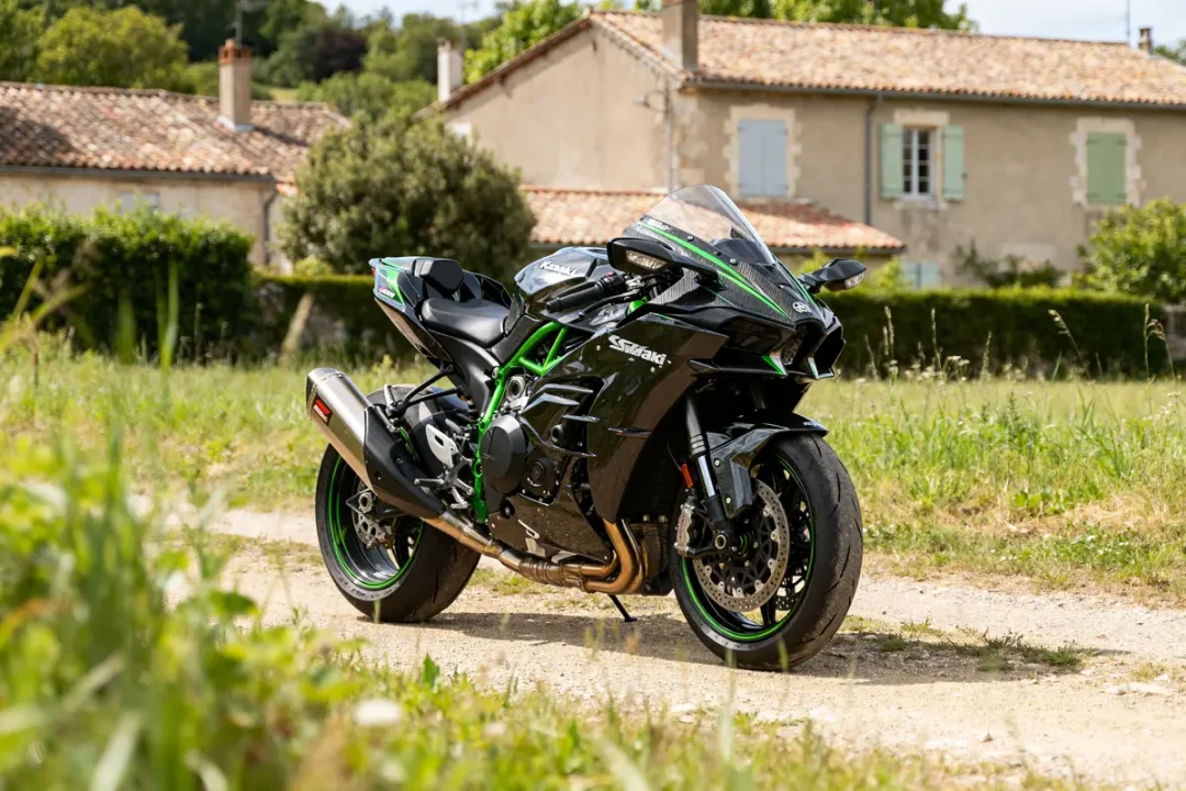Kawasaki Ninja H2R garée sur chemin devant maisons en campagne verdoyante