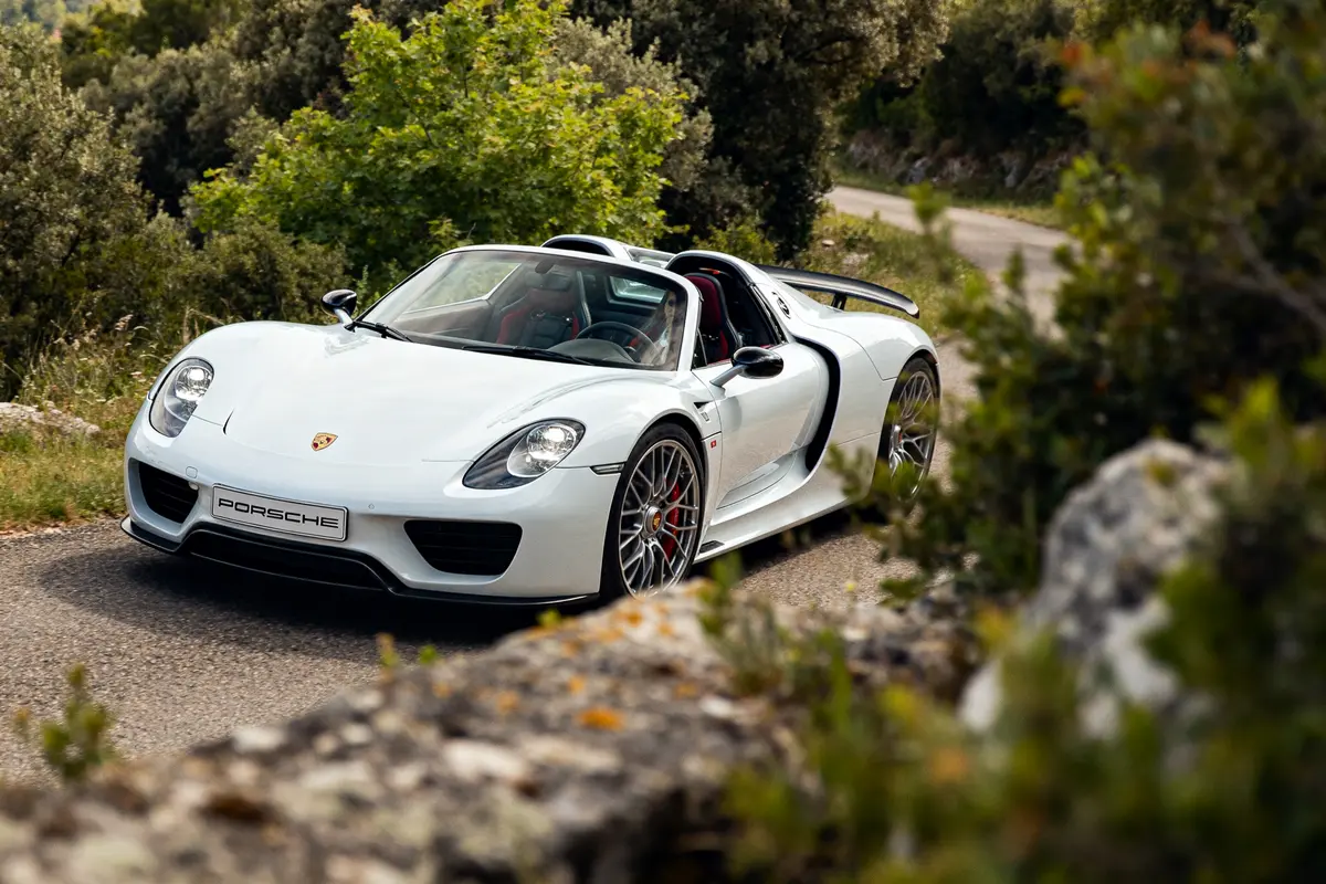 Supercar Porsche 918 Spyder blanche sur route de campagne avec verdure autour