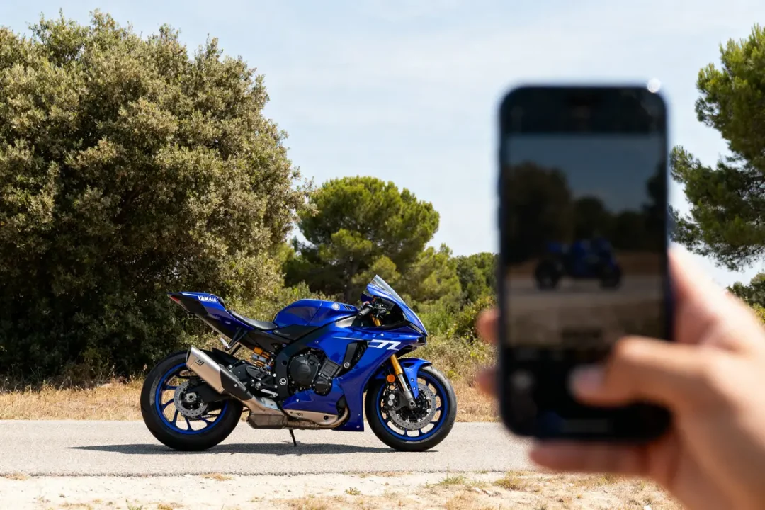 Moto Yamaha R7 bleue photographiée sur route ensoleillée avec smartphone flou au premier plan