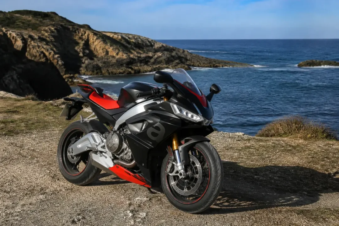 Moto Aprilia RS 660 noire, rouge en bord de mer avec falaises et océan背景