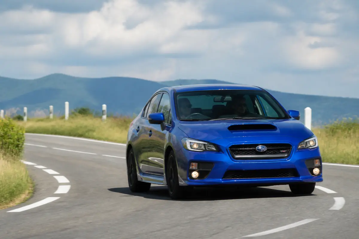 Voiture Subaru WRX sur route sinueuse devant paysage montagneux et ciel nuageux.